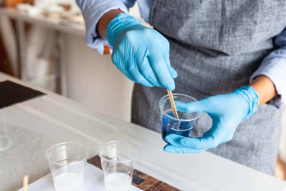 person with blue gloves mixing a cup of blue resin with a mixing stick