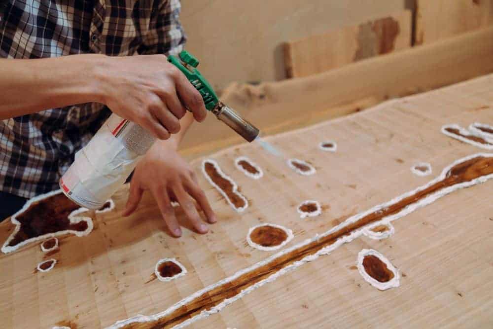 person in a checked shirt using a butane torch to remove resin bubbles from a wood surface 