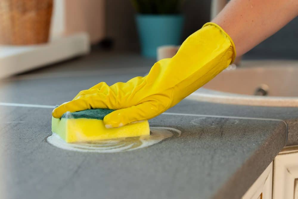 hand in a yellow rubber glove wiping a flat surface with a sponge