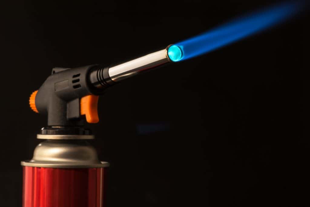 Butane torch with red cannister and black background shooting a blue flame 