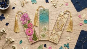 Three handmade resin bookmarks with pressed flowers, glitter ombre and gold monogram on wood