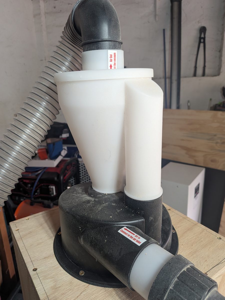 Close-up of a cyclone dust separator showing the Air In label on the side inlet and the Air Out label on the top outlet