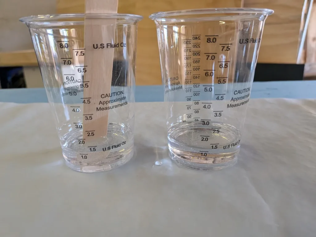 Two graduated mixing cups side by side, each holding 1 oz of clear epoxy, Part A and Part B filled to the same line
