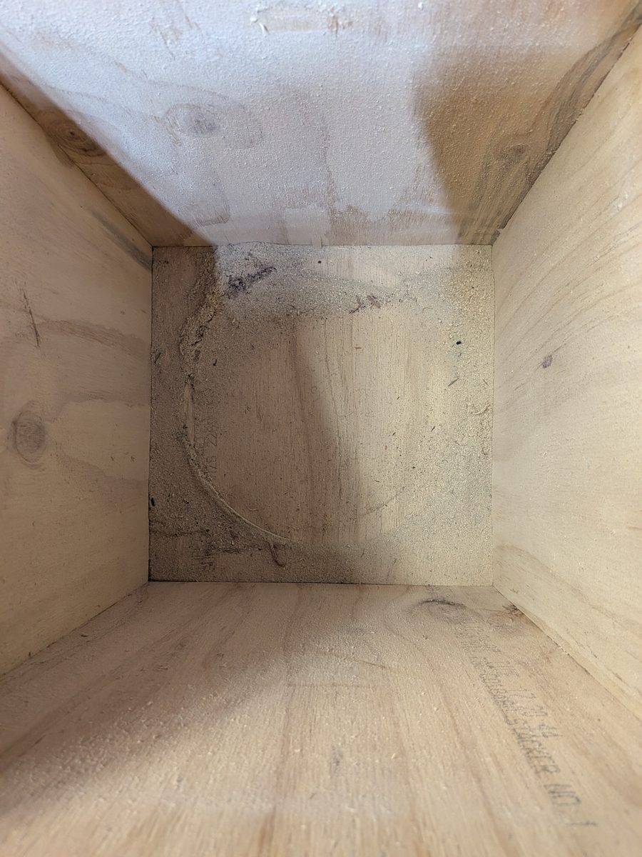Inside the empty plywood bin with a faint ring of fine dust where the bucket sat