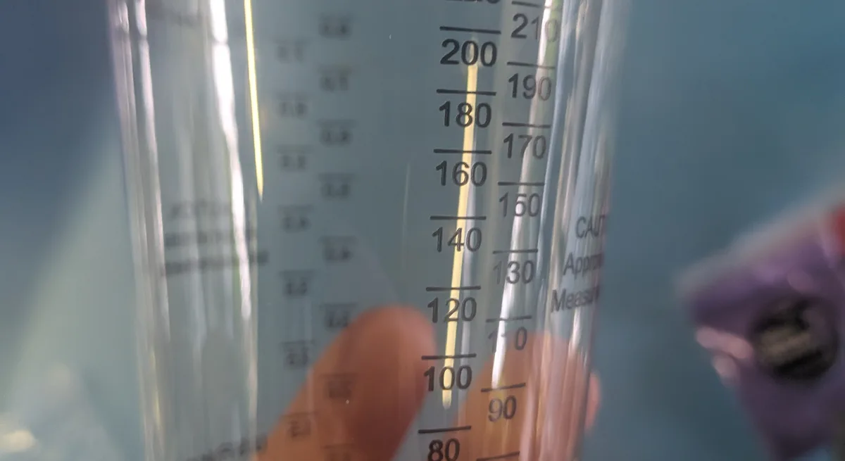 Close-up of a clear plastic mixing cup with graduated milliliter and cc markings