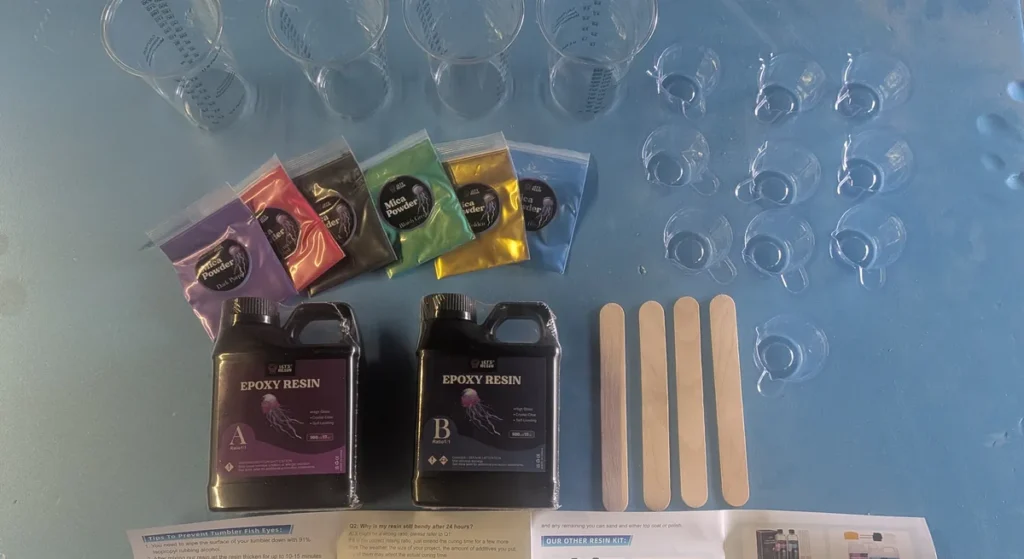 Let’s Resin epoxy starter kit laid out: Part A and Part B bottles, six mica powder bags, four graduated mixing cups, ten small pour cups and four wooden stir sticks