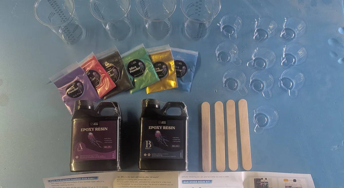 Let’s Resin epoxy starter kit laid out: Part A and Part B bottles, six mica powder bags, four graduated mixing cups, ten small pour cups and four wooden stir sticks