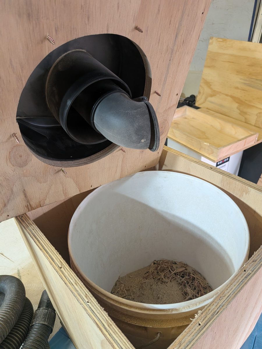 Plywood dust bin with the lid removed, showing the cyclone base through the lid and a bucket inside holding collected dust