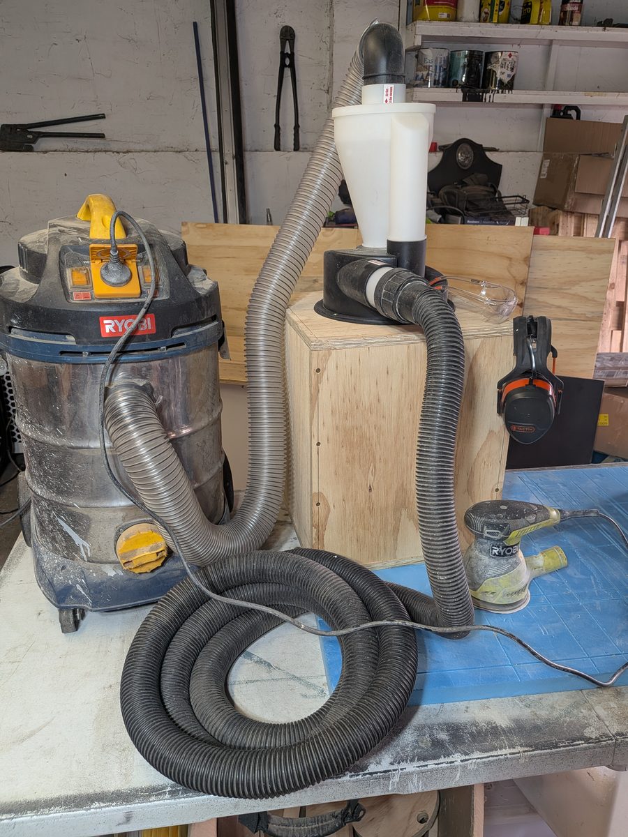 Complete dust collection setup: shop vac, grey hose to a cyclone separator on a plywood bin, black hose to a random orbital sander