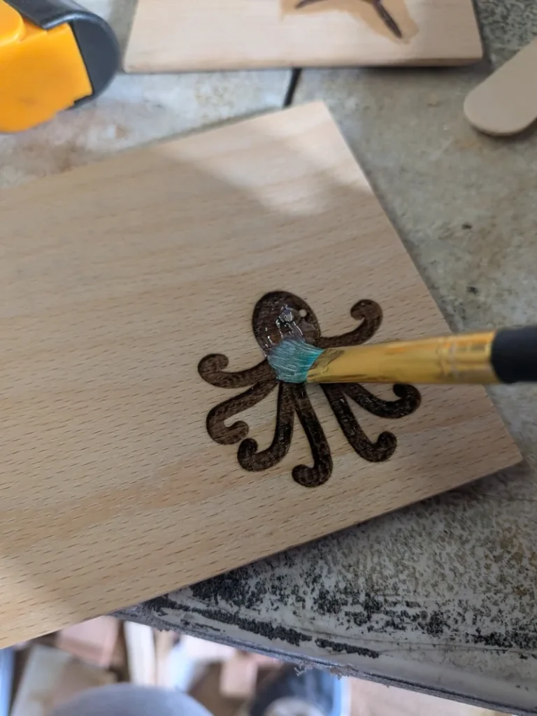 Brushing a thin seal coat of epoxy over a laser-engraved octopus on beech