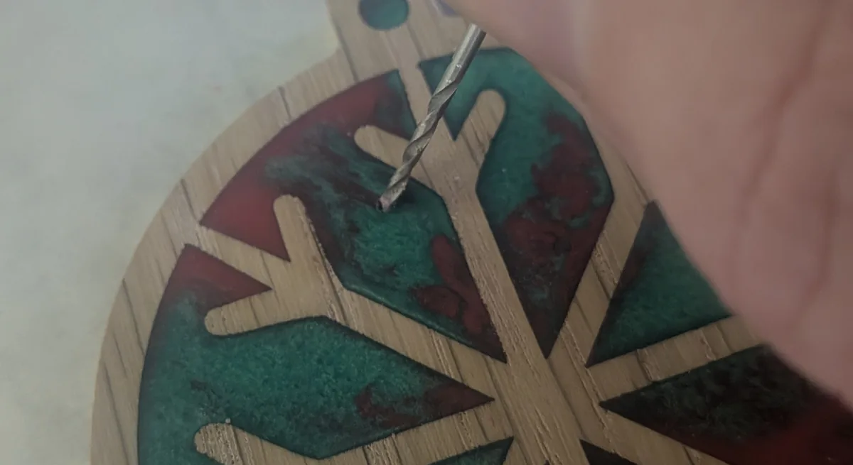 A small drill bit held by hand, clearing dust from a pinhole in cured teal resin