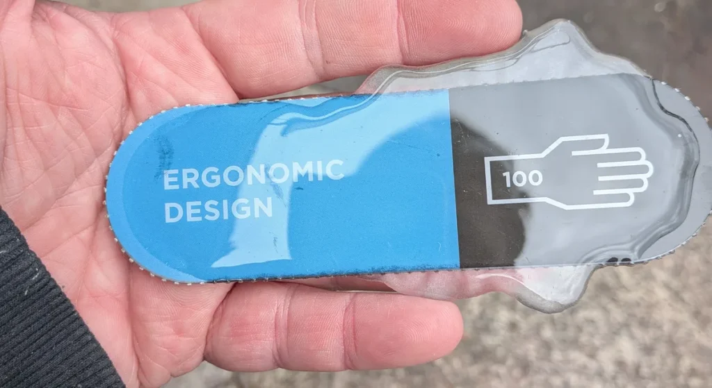 A cured pool of clear epoxy over printed cardboard held in an open hand, with the white lettering and a glove icon reading sharply through the resin