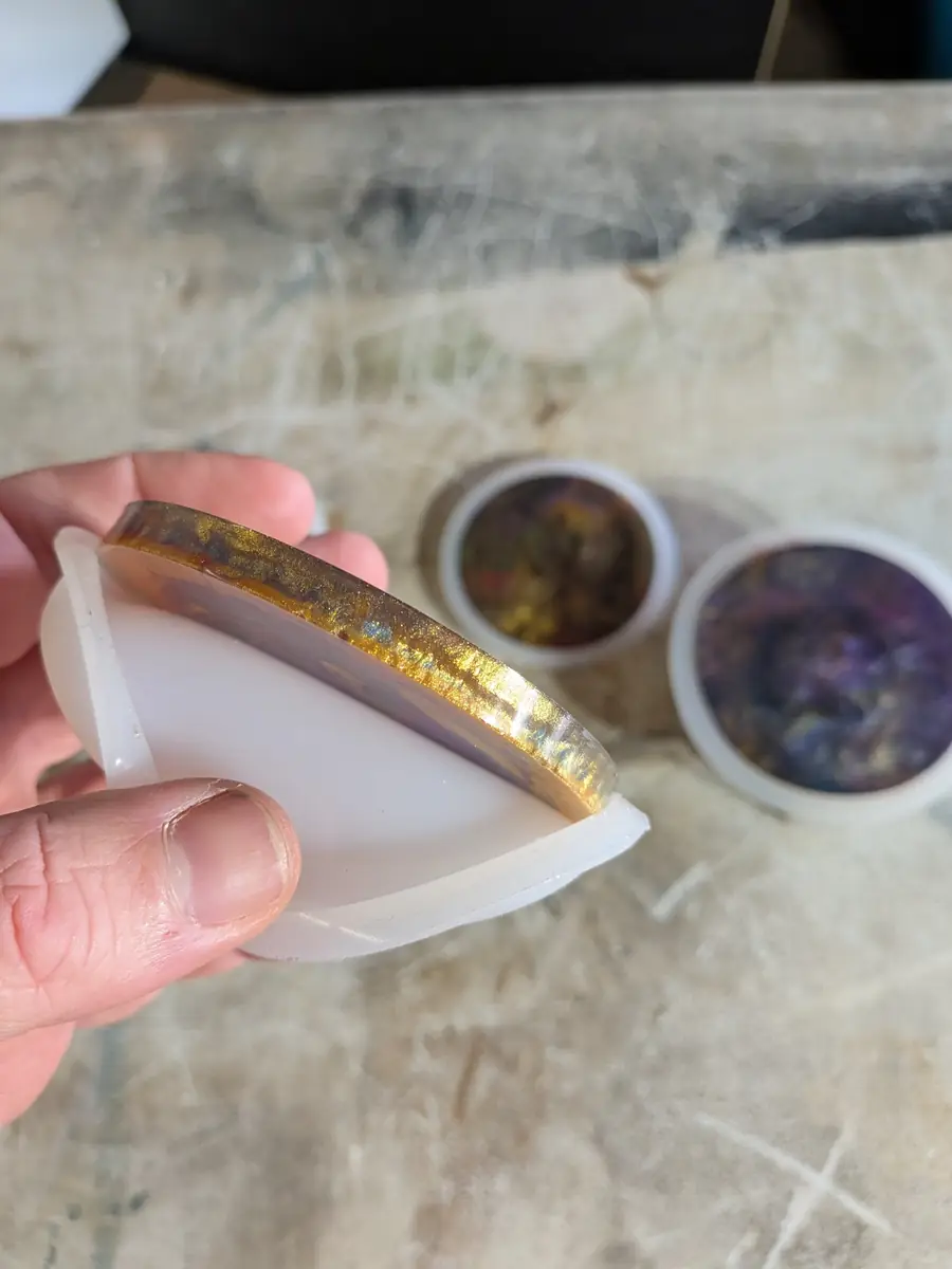 A cured gold-edged resin coaster being peeled out of its round silicone mold