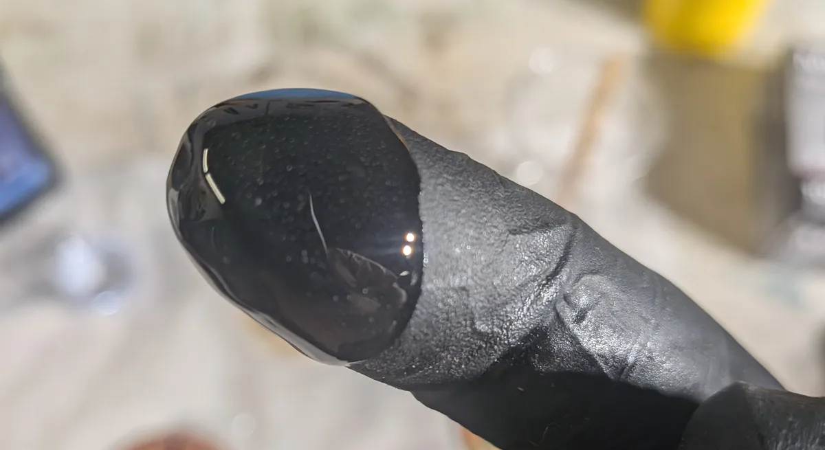 A drop of clear epoxy resin on the fingertip of a black nitrile glove