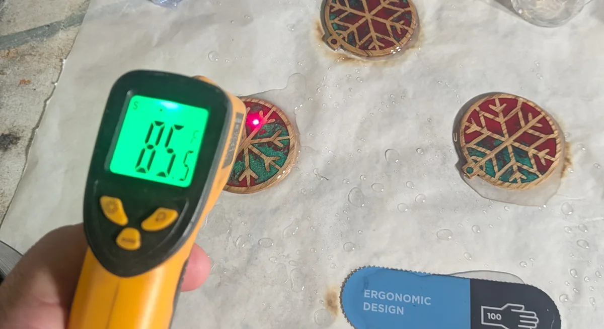An infrared thermometer reading 85.5°F aimed at freshly coated resin ornaments on a workbench
