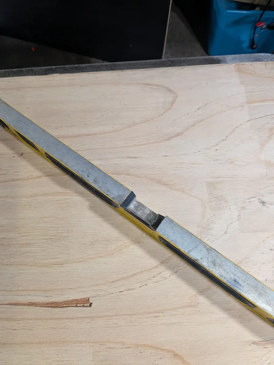 A spirit level laid across a plywood board to check the work surface is level before pouring resin coasters