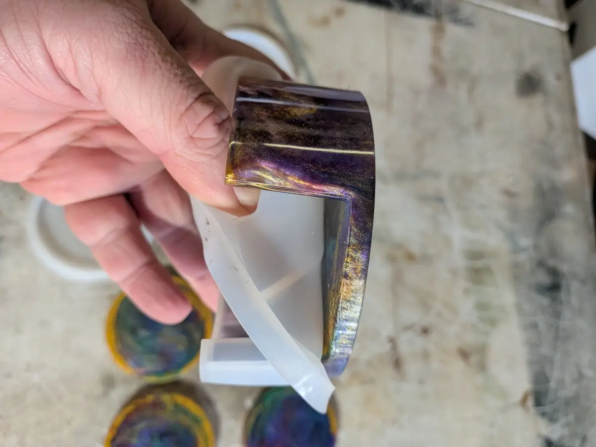 Peeling the silicone mold back from a cured purple and gold resin coaster holder