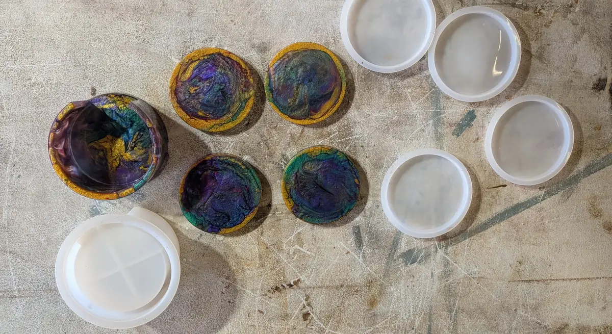 A finished resin coaster set, four swirled coasters and a slotted holder, laid out beside their empty silicone molds