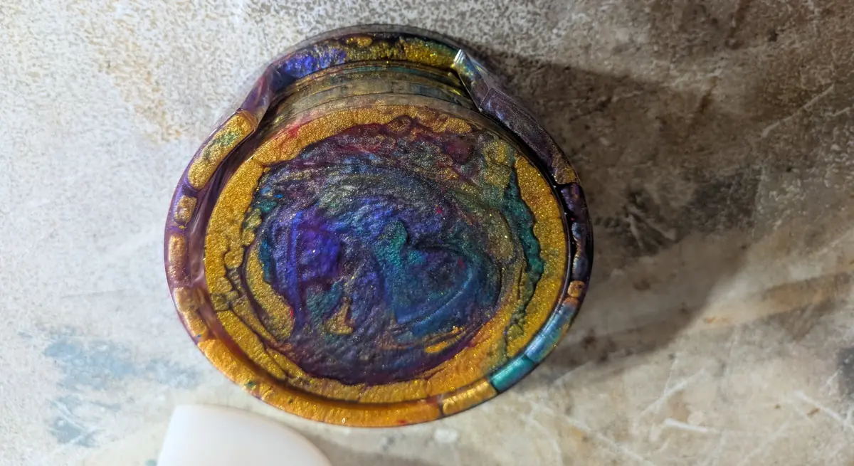 Four swirled purple, teal and gold epoxy resin coasters stacked in a matching resin holder, seen from above