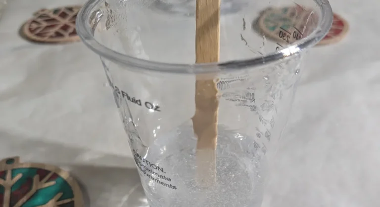 A clear mixing cup of freshly stirred epoxy resin, cloudy with fine bubbles, with a wooden stir stick standing in it