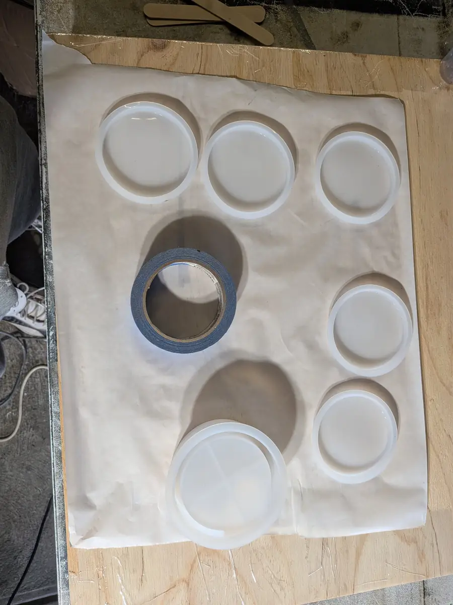 Round silicone coaster molds laid out on baking paper over a levelled board, ready for the pour