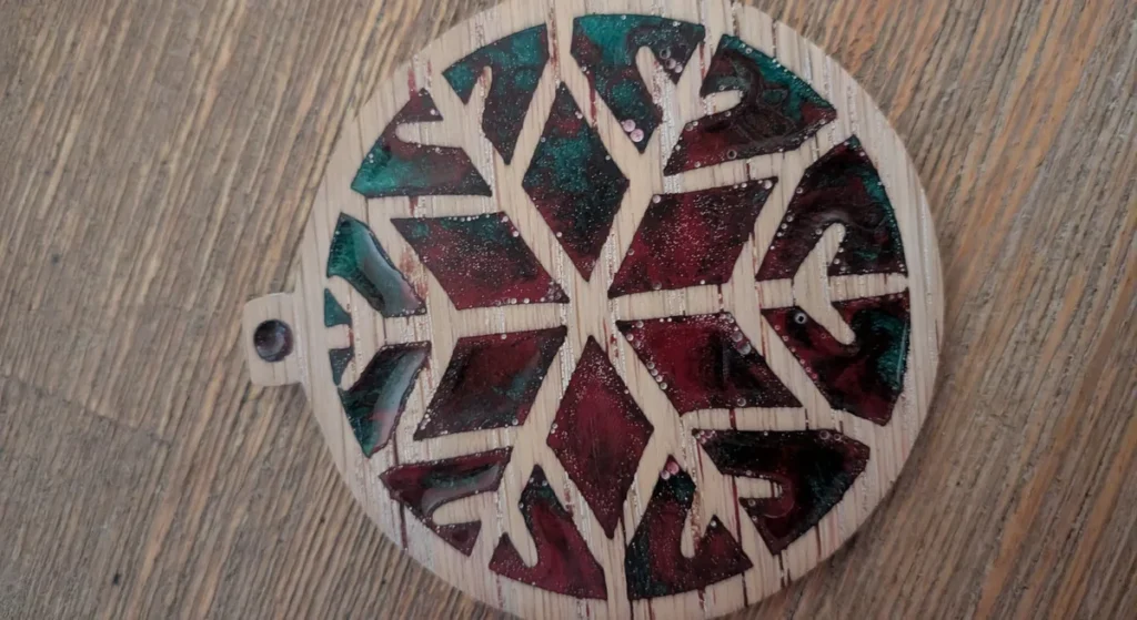 A sanded wooden snowflake ornament filled with red and green resin, with small white dots where sanding opened bubbles just under the surface