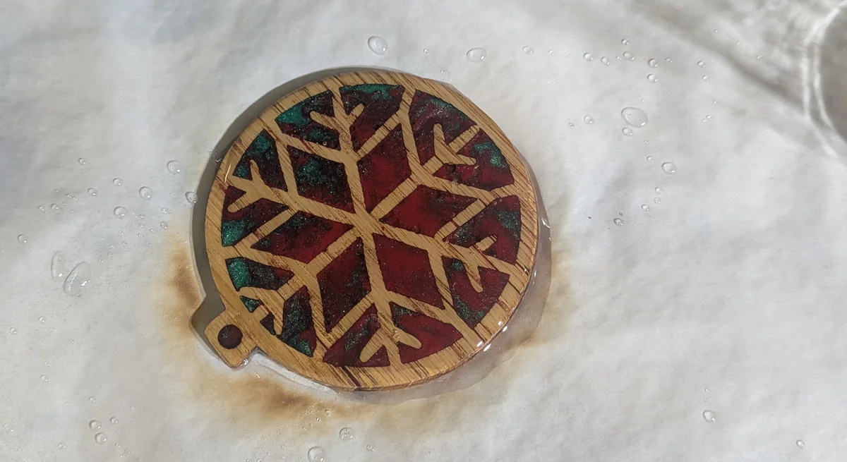 A resin-filled wooden ornament with a wet clear coat, and baking paper scorched brown around it by a torch