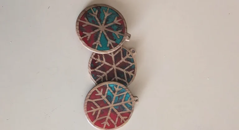 Three laser-cut wooden snowflake ornaments filled with red and teal resin